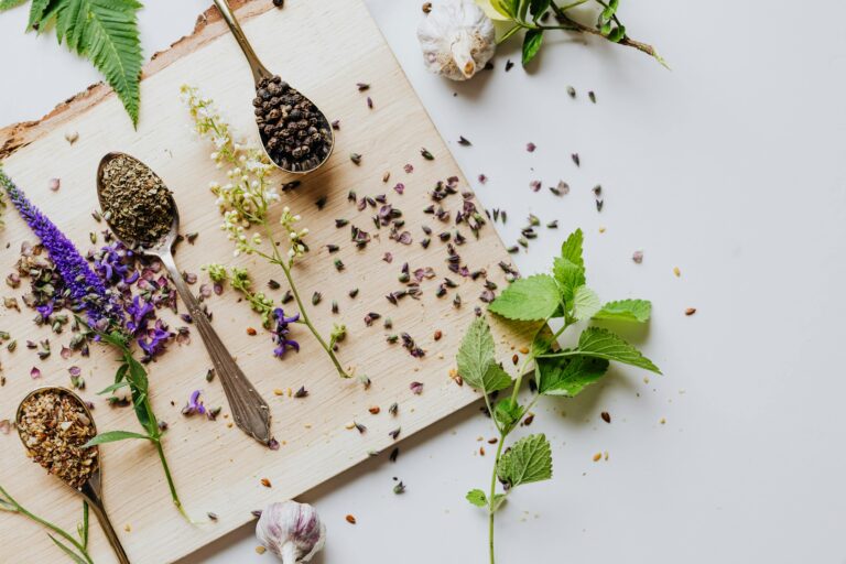 Overhead shot of herbs and spices on a wooden chopping board with spoons, showcasing culinary ingredients.